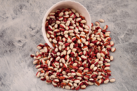 Raw beans crumbled from a white round bowl onto a wooden background.