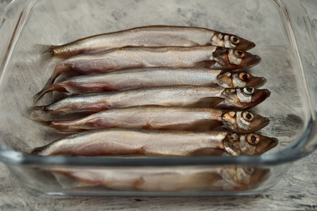 Whole small fish on the bottom of the glass container, wooden background.の写真素材