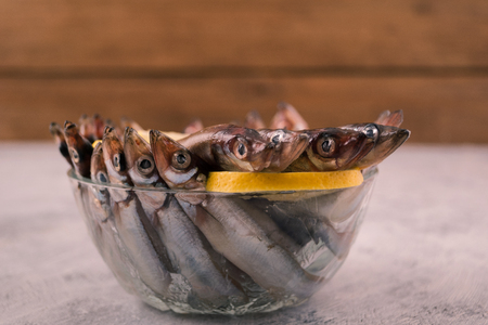 Fresh capelin, small sea fish, with a slice of lemon in a round glass bowl.の写真素材