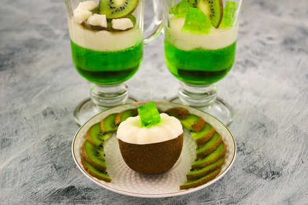 Sliced kiwi with white and green jelly. Glasses of gelatin and kiwi slices. Exotic Chinese fruit. Vegetarian food. Light background.の写真素材