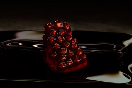 Part of a ripe pomegranate. Red grains with seeds. Juicy shiny seeds. Black glass plate. Tropical fruit.の写真素材