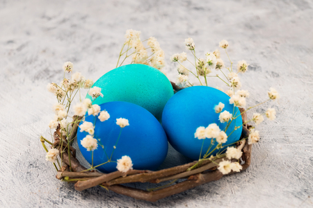Easter eggs closeup in a nest from branches. White small flowers on a light background. Easter decoration.の写真素材