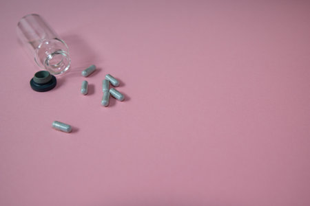 Pills spilling out of pill bottle on pink background with copy spaceの写真素材