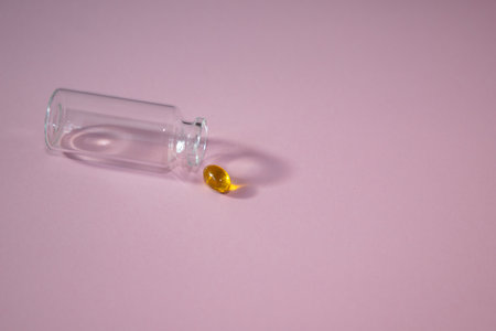 A small transparent bottle with a yellow pill on a pink background.の写真素材