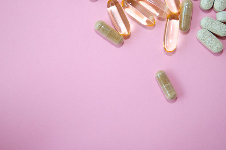 Pills and capsules on pink background. Top view with copy space