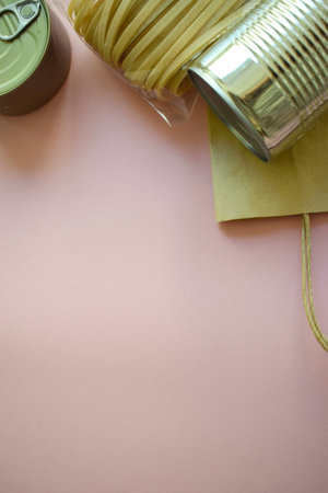 Top view of canned food and pasta in a paper eco bag placed along the top border on a pink vertical background. Copy space below. Ideal for food delivery, zero waste, or groceryの写真素材