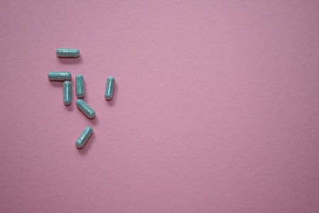 Capsules are scattered across a soft pink background, highlighting their unique shapes and colors,...
