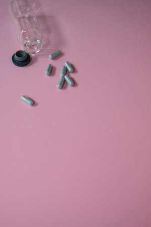 Glass bottle spills light green capsules onto a soft pink surface, creating a serene and inviting...