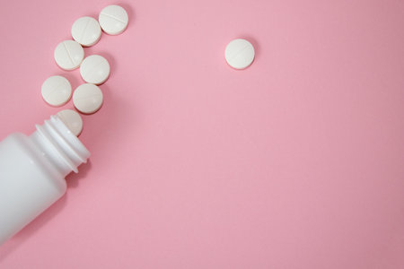 White tablets are scattered from a bottle against a pink backdrop, emphasizing a clean and modern...
