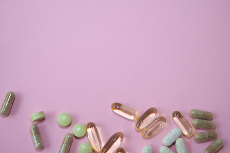 Various dietary supplements including capsules and tablets are scattered on a soft pink background,...