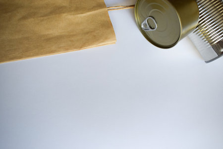 A metal can with a pull tab is positioned next to a brown paper bag on a white background, showing a...