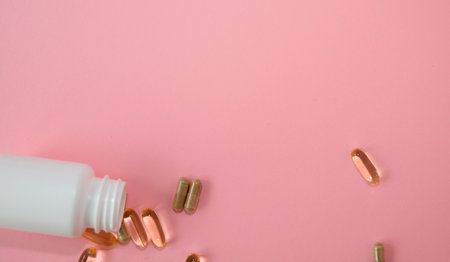 White bottle is spilling capsules on a pink background, highlighting dietary supplements and health...