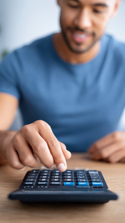 Man operates a calculator for budgeting and financial planning on a wooden table, with soft lighting creating a calm atmosphere in the backgroundの素材