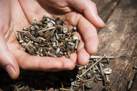 iron rusty tools bolts and screws in his hands on an old wooden table close-up selective focusの写真素材