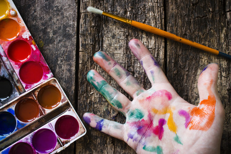 watercolor paint brush to paint the hand of the artist in multi-colored paint on wood backgroundの写真素材