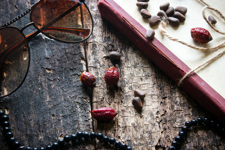 glasses, beads, books, nuts, rose hips on a wooden background closeupの写真素材