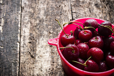 Rural berry cherry with drops of water in a red bucket on a wooden tableの写真素材