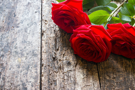 Three red roses on a wooden background with the stem and leavesの写真素材