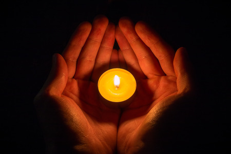hands in the shape of a heart holding a lighted candle on a black backgroundの写真素材