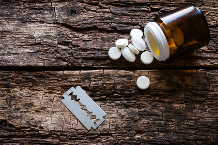 handful of pills and a blade on wooden backgroundの写真素材
