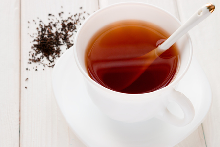 tea in a white mug with a spoon and tea leaves on a white backgroundの写真素材