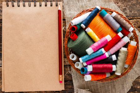 notebook and a basket with colored thread for sewing