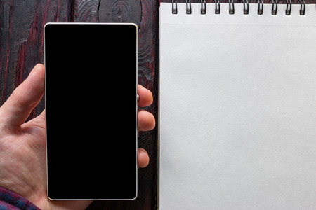 man holding the phone next to the white notebook