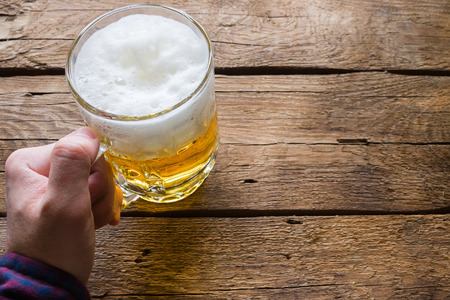 man holding a glass of beer on a wooden backgroundの写真素材