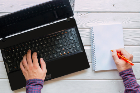man working at the computer and writing in a notebook on a white wooden backgroundの写真素材