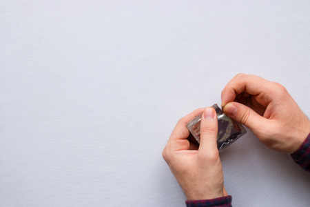 man opens a condom on a white background with space for textの写真素材