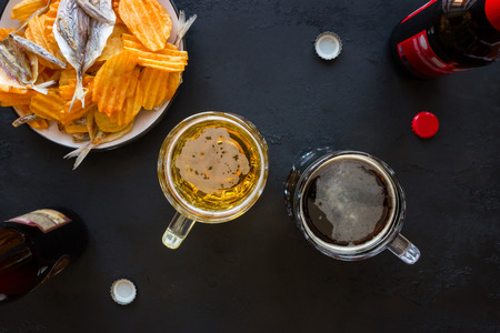 Mugs with beer, bottles and snacks on a black backgroundの写真素材