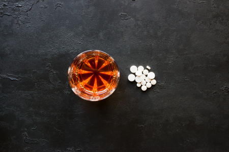 Alcohol in a glass and a handful of pills on a black backgroundの写真素材