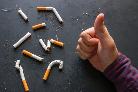 Man shows his thumb against the background of broken cigarettes - stop smokingの写真素材