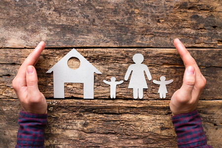 male hands and paper silhouettes of his wife and children near the house. concept of protection and careの写真素材