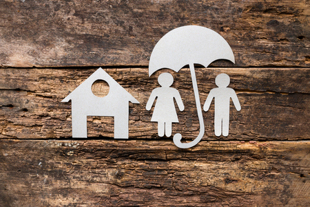 husband and wife under an umbrella near the house on a wooden backgroundの写真素材