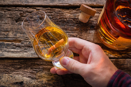 hand holds whiskey in a glass for tasting on a wooden backgroundの写真素材