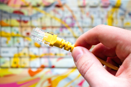 man holds yellow network internet cable on laptop background