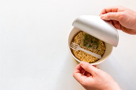 man opens the box with instant noodles on a white background with space for textの写真素材