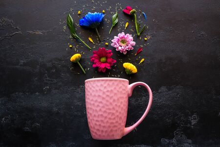 pink mug and a scattering of flowers and petals from it on a black background top viewの写真素材