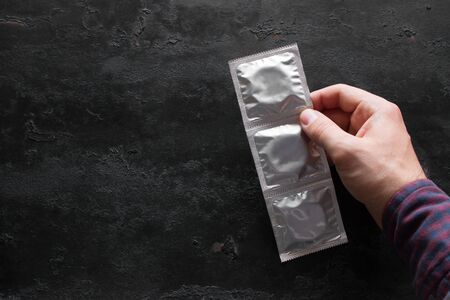 hand holds packing of condoms on black background with place for text.