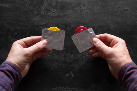 man holding open yellow and red condoms on black background. concept contraceptionの写真素材