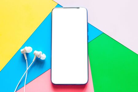 mobile phone smartphone with a blank white screen and headphones on a colored background mockupの写真素材