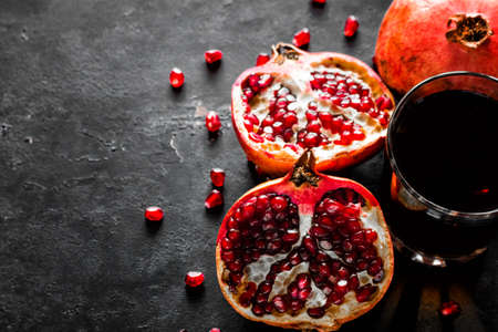 pomegranate juice in a glass and pomegranate with seeds on a black background with place for text