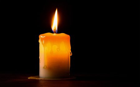 yellow burning candle with dripping wax on wooden tableの素材
