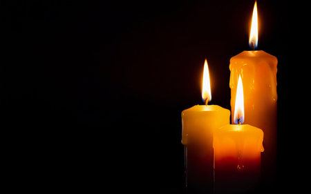 three yellow burning wax candles on a black background with space for textの素材