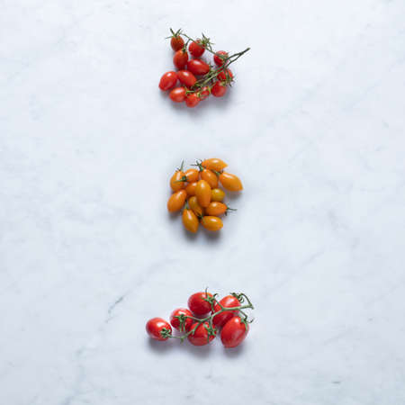 Tomatoes from Italy, Isolated on Marble Background - Bunch of Italian Cherry Tomatoes, Orange or Yellow Variety, with Branch, Twig, Three Groups - Close-Up Macro, Top View, from Aboveの写真素材
