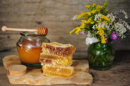 Honey in honeycombs and a barrel of honey or a wooden stick, tea with honey and lemon on a wooden backgroundの写真素材