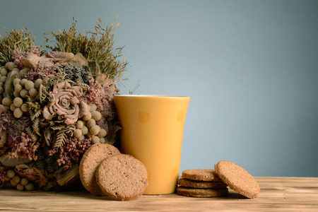 Mug of milk and cookies on vintage wooden background with dried flower bouquet