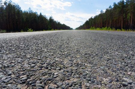Straight asphalt road and green forest under blue sky. Empty scenic highway with natural scenery through the trees background.の写真素材