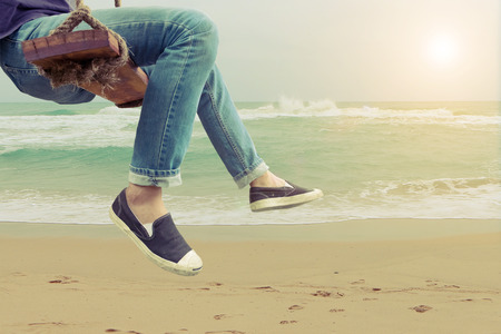 Hipster man sitting on swing in the beach on summer sun. Vintage filter effect.の写真素材